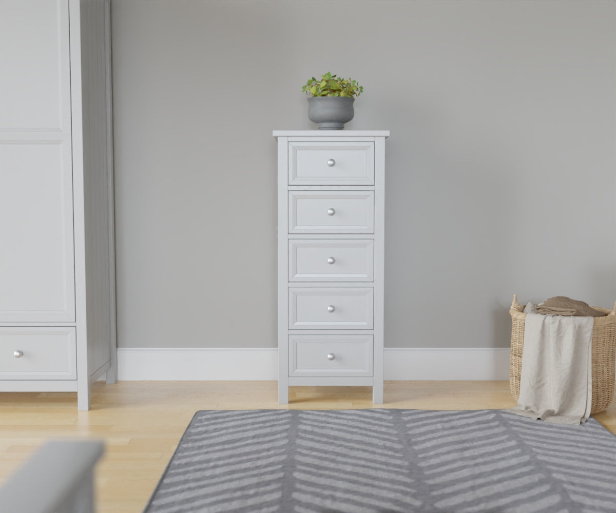 Maine 5 Drawer Chest in grey has a square-edged top, with 5 equal vertical drawers with round handles. This lifestyle image features other products from the Julian Bowen Maine range.